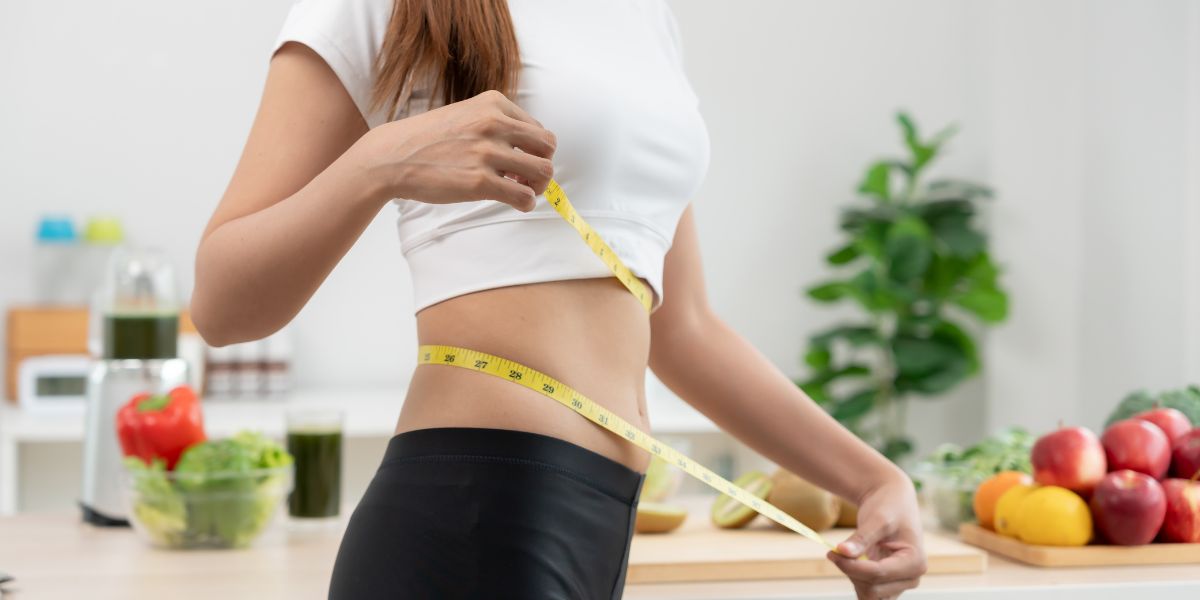 ウエストをメジャーで測る女性。糖質を削りすぎない見直しとして、トレ前後は少量の主食+タンパク質、1種目1セットOKで継続するイメージ。