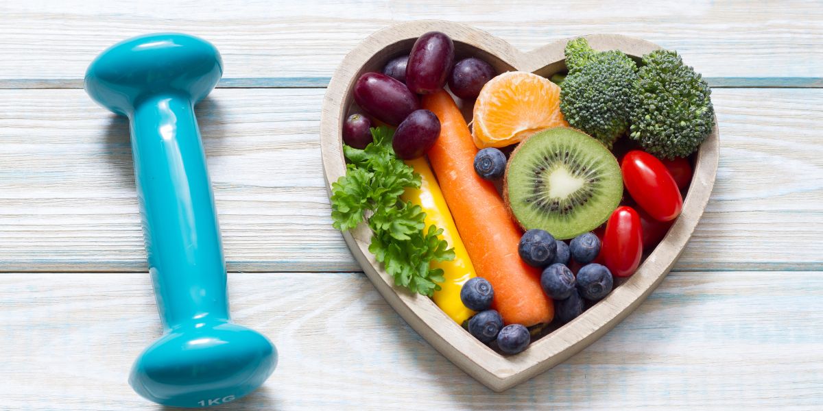 ダンベルとハート型ボウルの野菜果物。食事と運動をセットにして続ける“7分/15分+週の型”のイメージ。40〜50代女性向け。