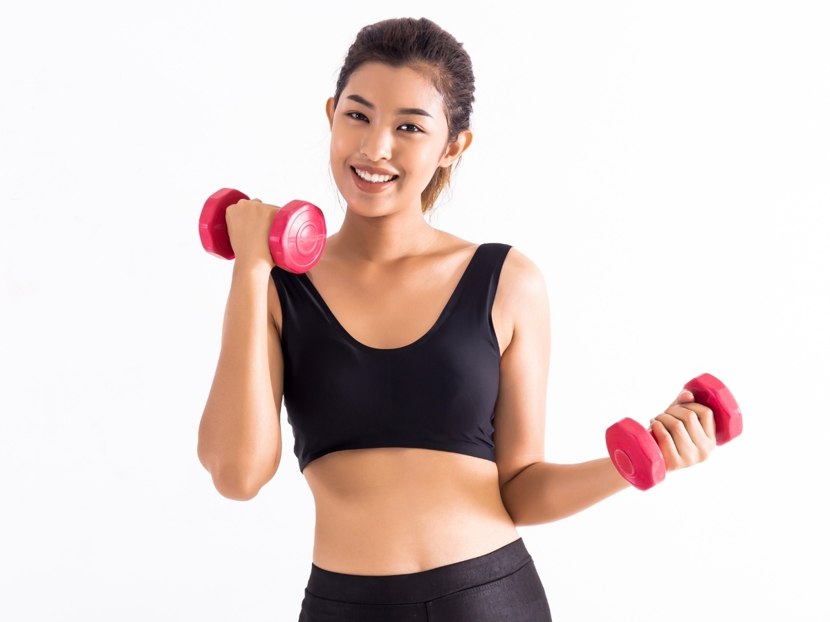 ピンクのダンベルを持って笑顔でトレーニングする女性のイメージ